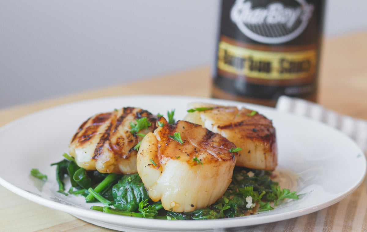 Seared scallops on wilted spinach beside a bottle of CharBoy's Bourbon Sauce