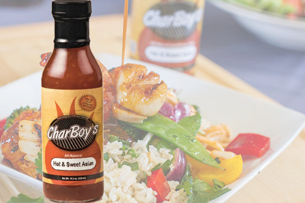 A bottle of CharBoy's Hot & Sweet Asian Sauce beside seared scallops and rice