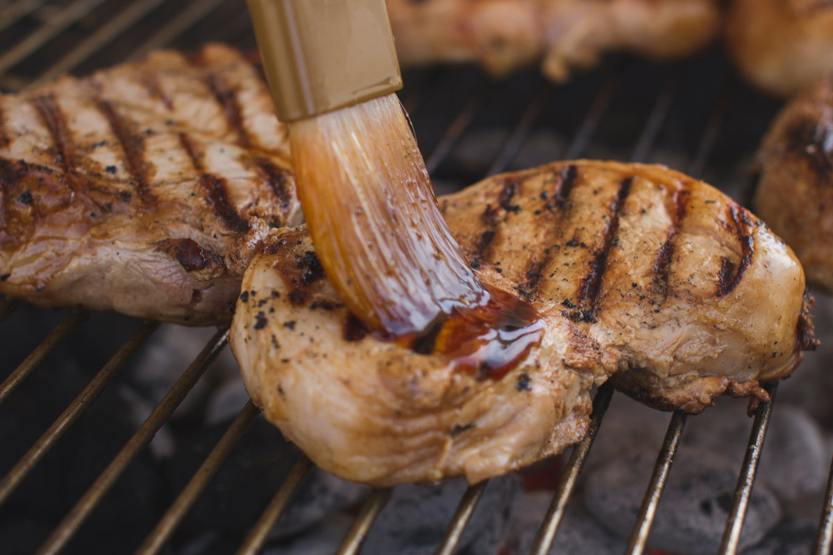 Grilled chicken being basted with CharBoy's sauce