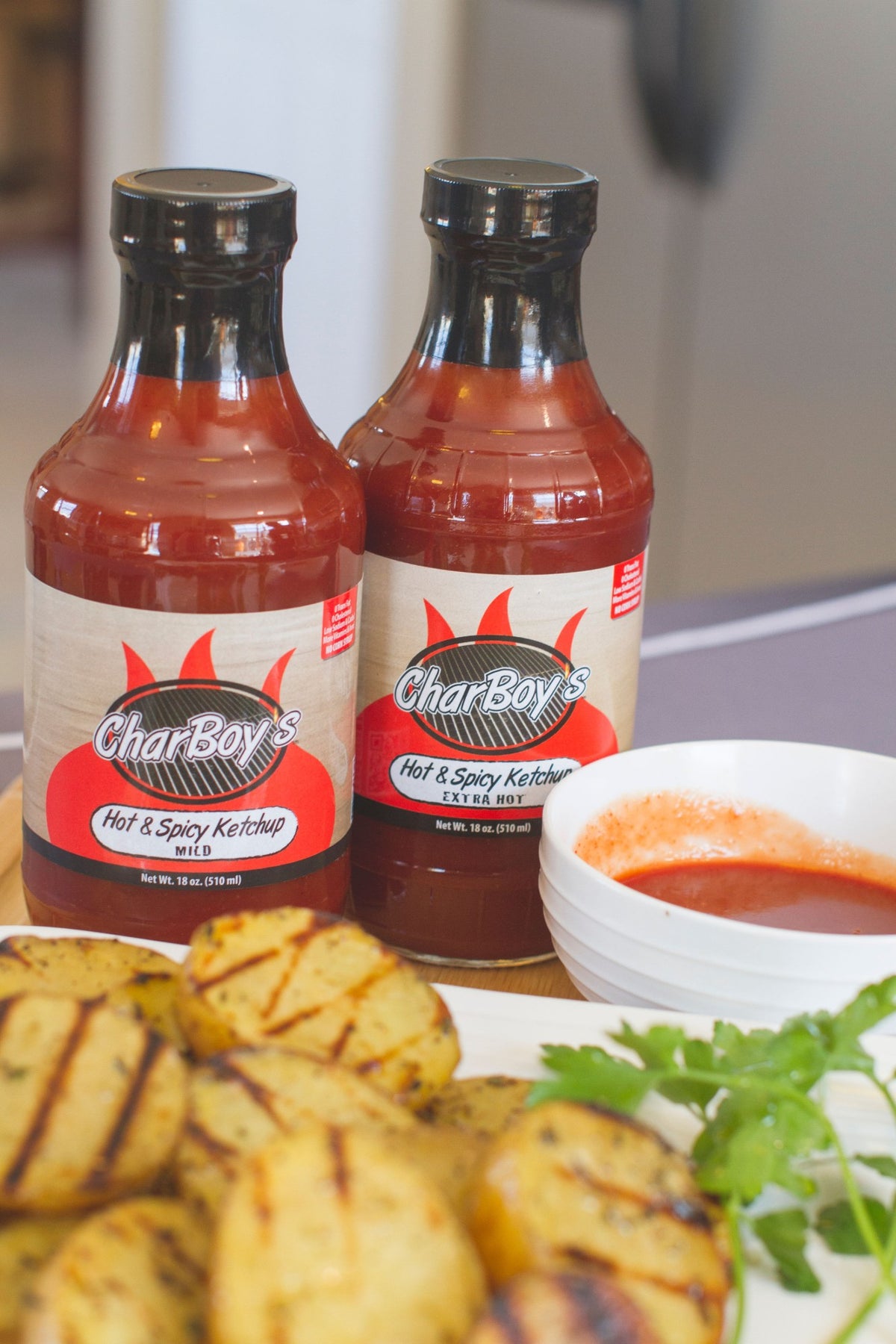 CharBoy's Hot & Spicy Ketchup Mild and Extra Hot bottles with grilled potatoes and a bowl of ketchup