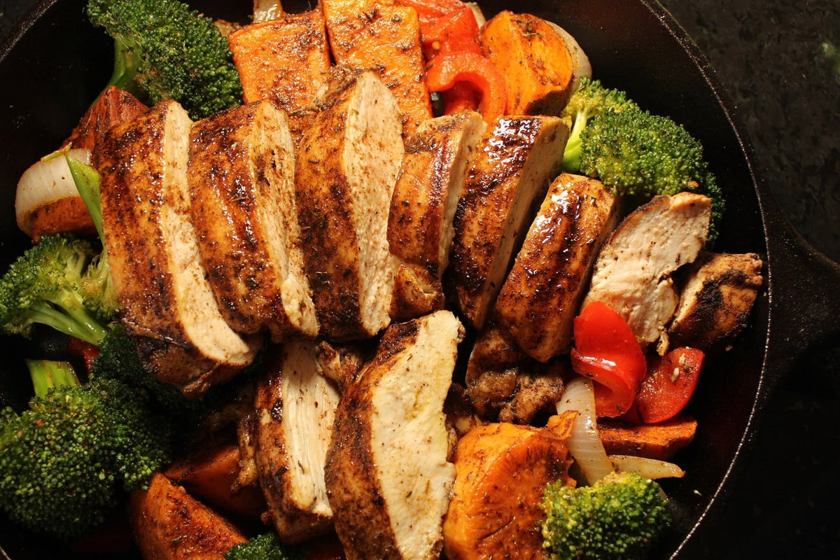 Jerk chicken sliced over a skillet of sweet potatoes, peppers, onion and broccoli